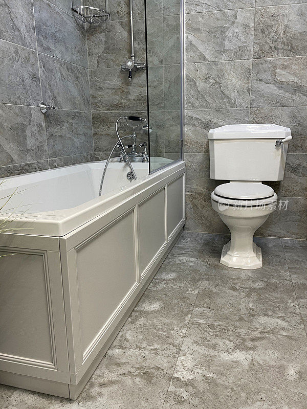 白色/灰色大理石墙砖的豪华浴室套房，白色陶瓷浴缸，镀铬维多利亚式龙头和淋浴管道，玻璃淋浴屏，手柄冲水马桶